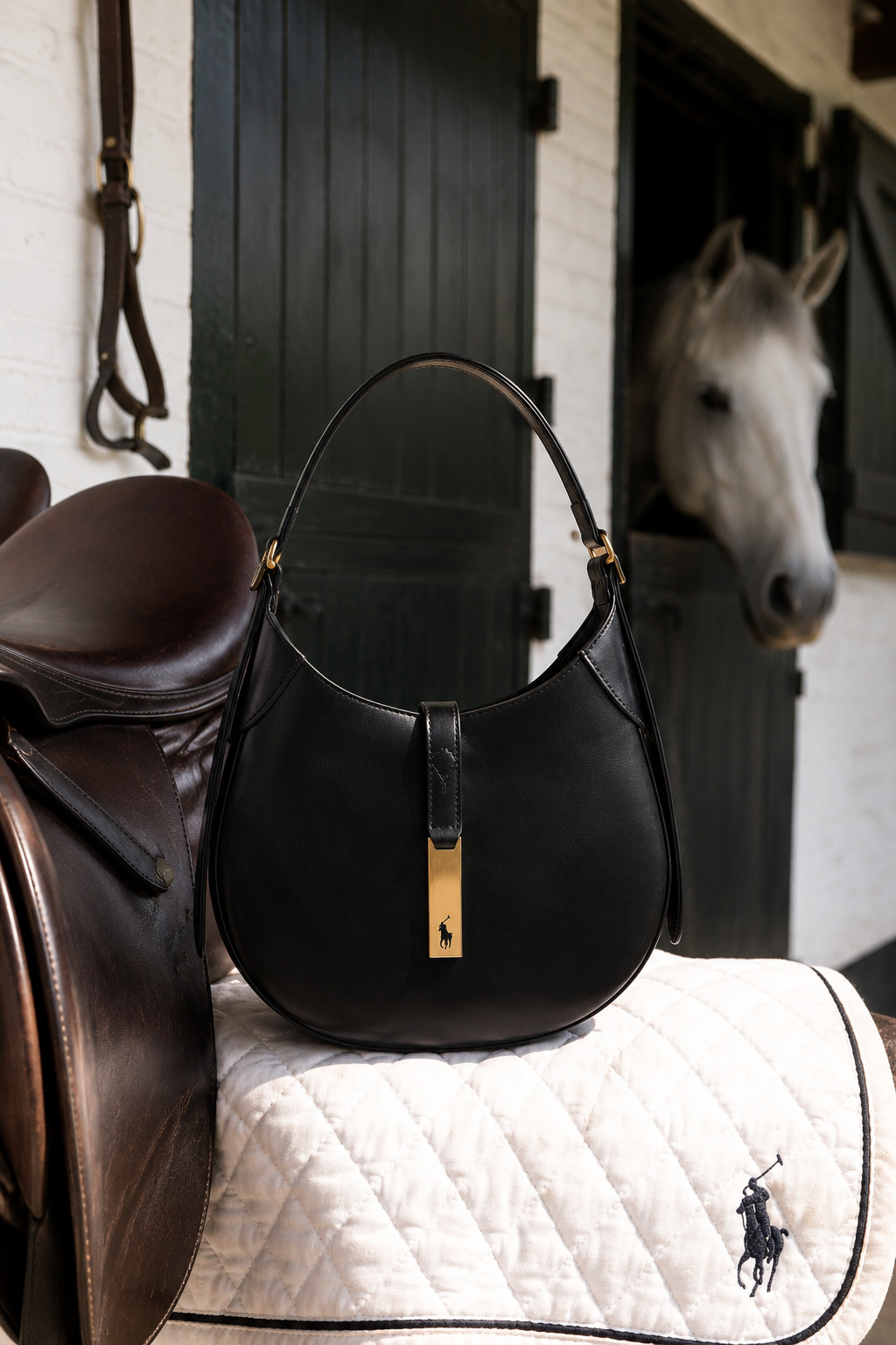 Black leather handbag on saddle padding inside a stable with a white horse