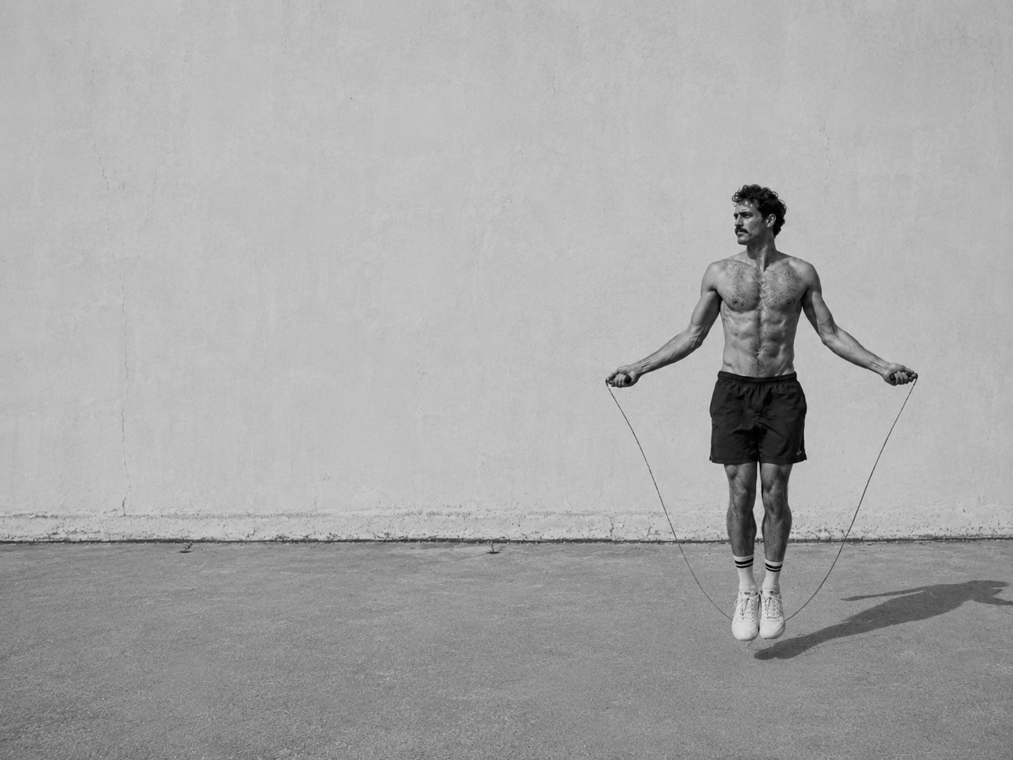 Black-and-white fitness campaign image of a man skipping rope against a concrete wall