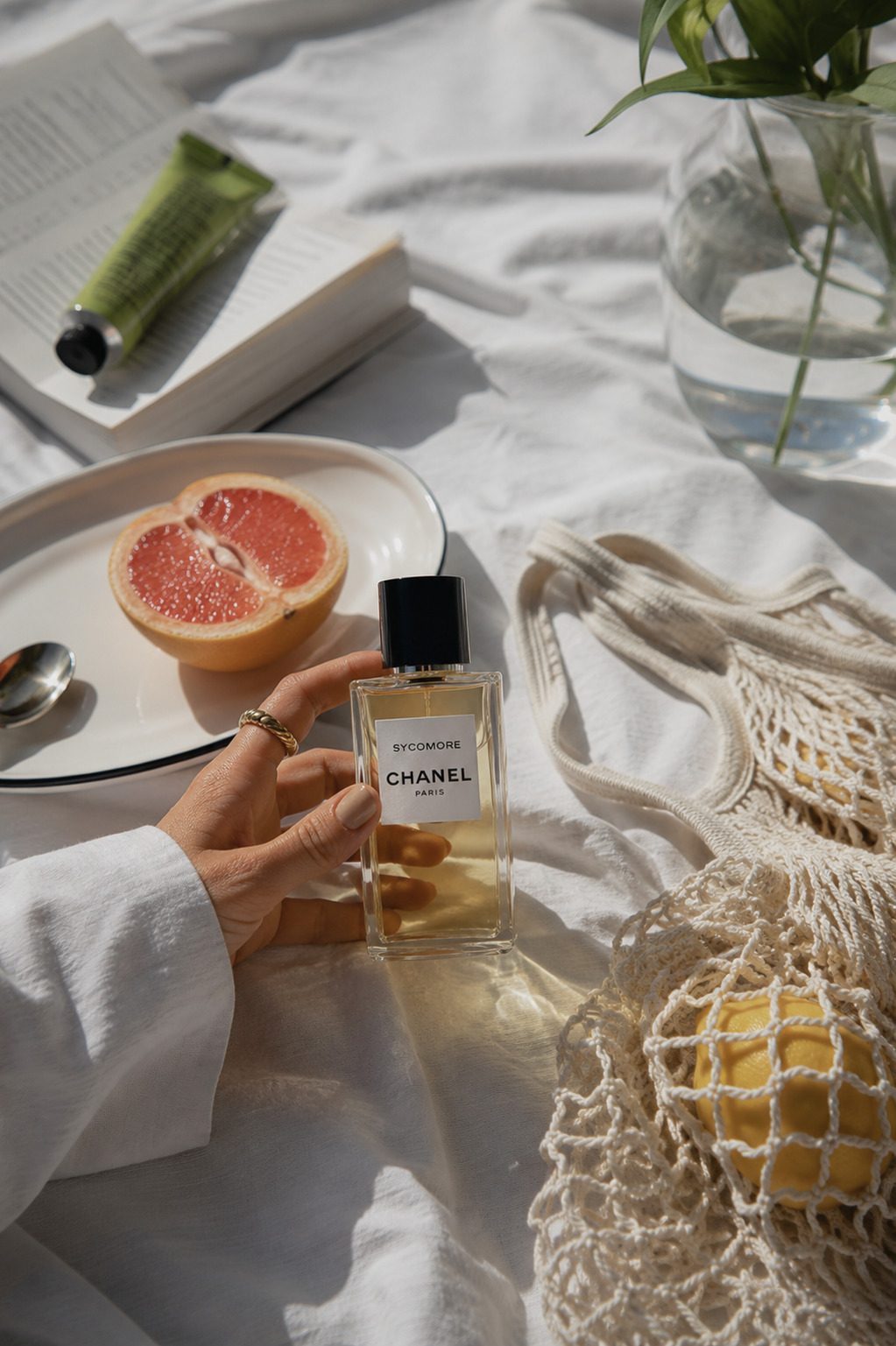 Hand holding Chanel perfume above cream bedding with grapefruit and breakfast styling