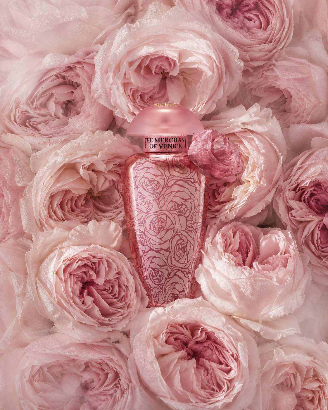 Pink perfume bottle surrounded by layers of soft pink roses