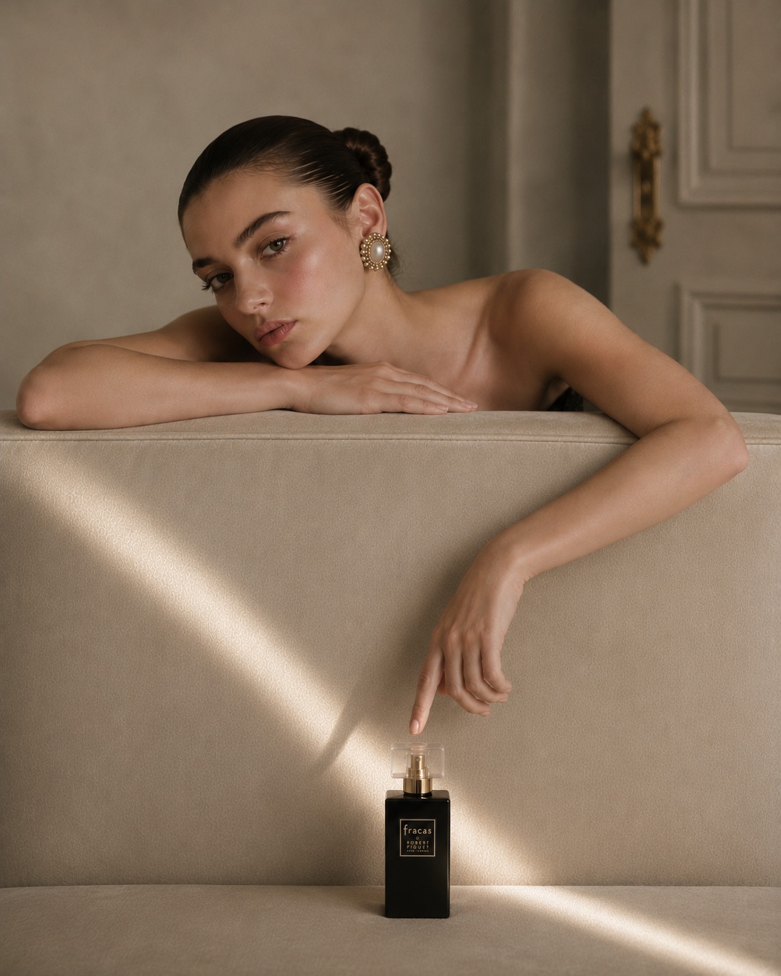 Model leaning over a cream plinth beside a Robert Piguet Fracas perfume bottle in sunlight