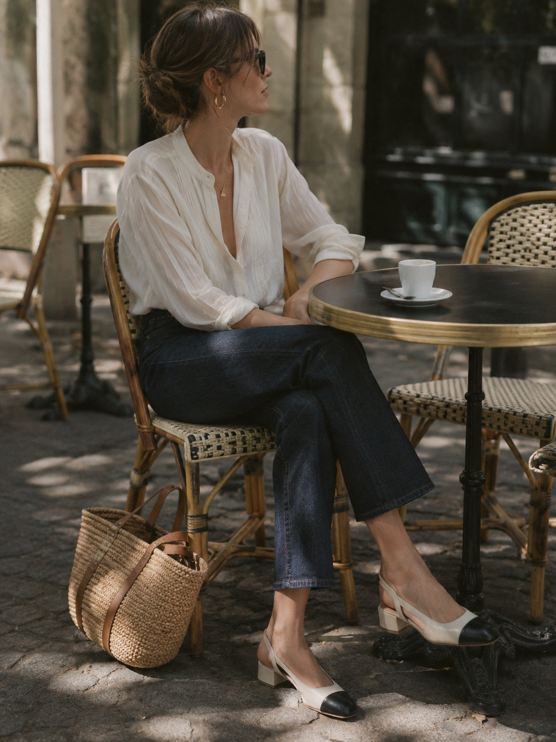 Woman seated at an outdoor cafe in a white blouse, jeans and neutral flats